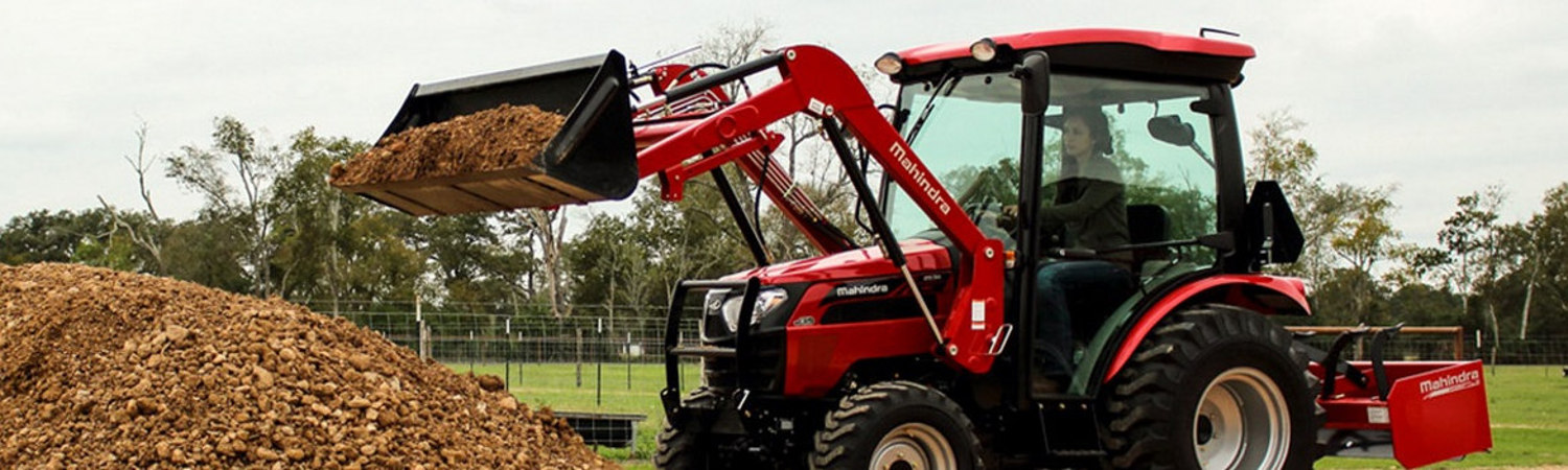 Woman in a Mahindra 2538CL tractor dumping dirt and rocks into a pile on a property